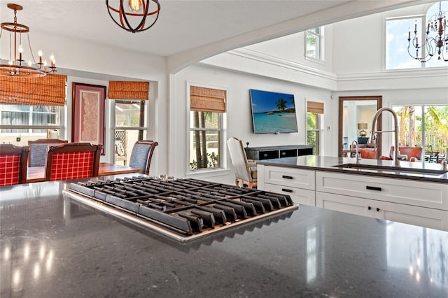 kitchen with white cabinets, a sink, dark stone countertops, a notable chandelier, and gas stovetop