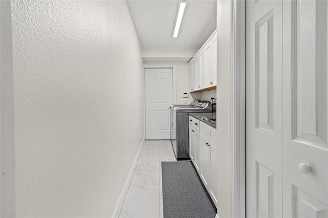 clothes washing area with baseboards, separate washer and dryer, marble finish floor, cabinet space, and a textured wall