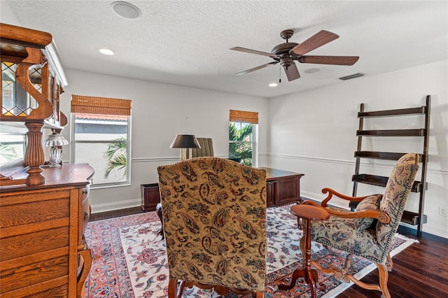 living area with wood finished floors, visible vents, a ceiling fan, and baseboards