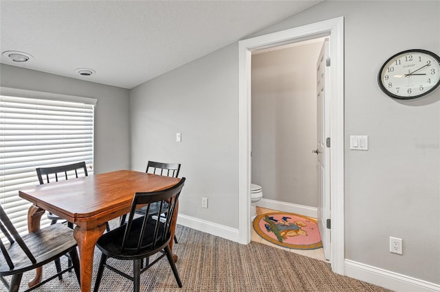 carpeted dining space featuring vaulted ceiling and baseboards