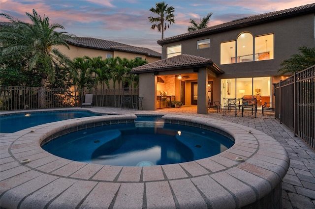 pool at dusk with fence, a patio area, outdoor dry bar, and a pool with connected hot tub