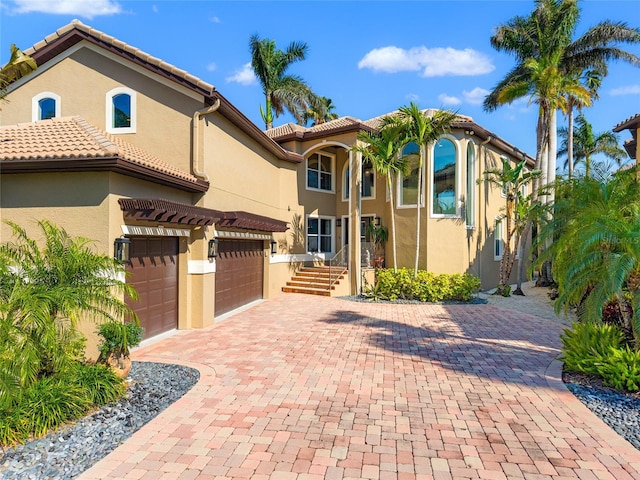 mediterranean / spanish home with an attached garage, a tiled roof, decorative driveway, and stucco siding