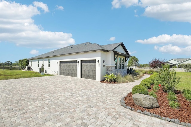 view of side of home with fence, an attached garage, a lawn, stucco siding, and decorative driveway