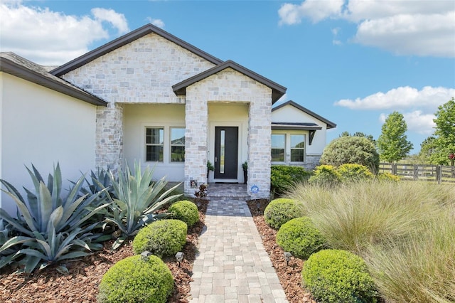 view of front of house featuring stucco siding, stone siding, and fence