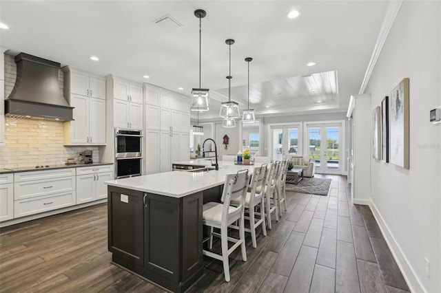 kitchen featuring a sink, stainless steel double oven, premium range hood, backsplash, and ornamental molding