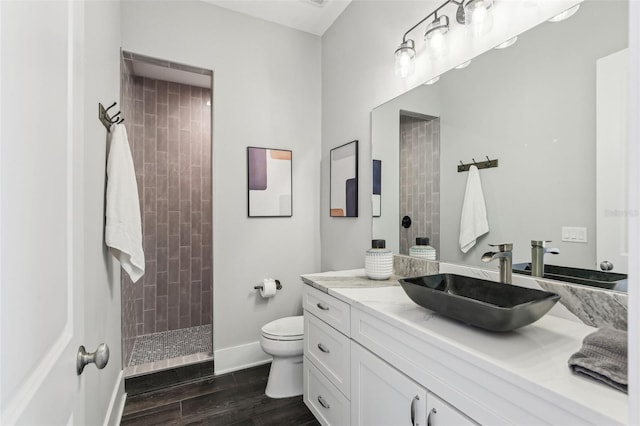 full bath with wood finished floors, toilet, vanity, baseboards, and tiled shower