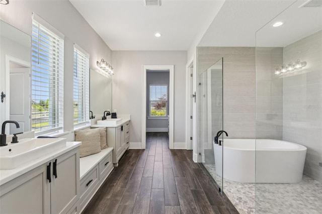 bathroom with a soaking tub, a sink, two vanities, wood finished floors, and a shower stall