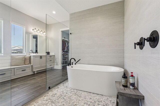 bathroom with a freestanding bath, tile walls, wood finished floors, vanity, and a walk in closet