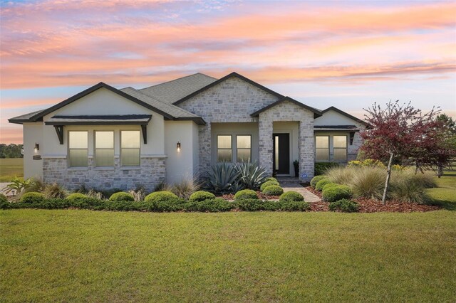 view of front facade with a yard, stone siding, and stucco siding