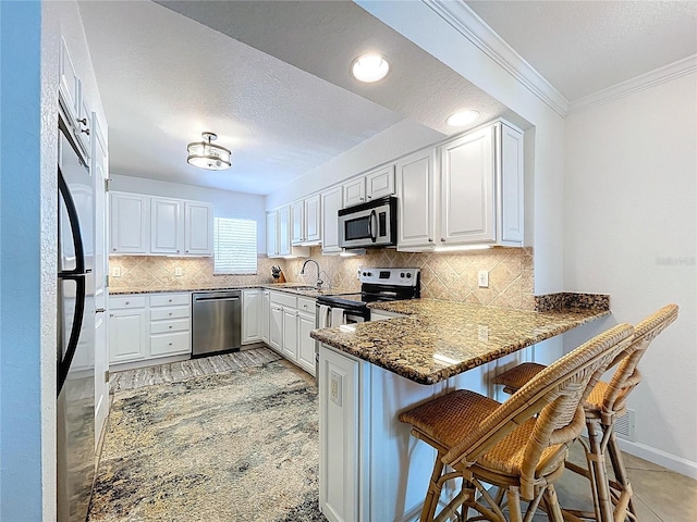 kitchen featuring a kitchen breakfast bar, white cabinets, a peninsula, ornamental molding, and stainless steel appliances