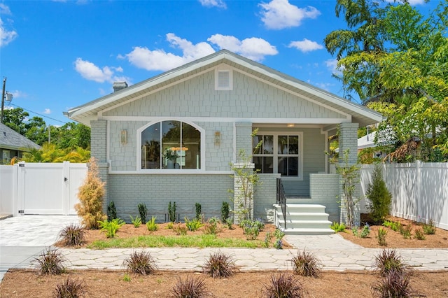 bungalow featuring a porch, fence, a gate, and brick siding