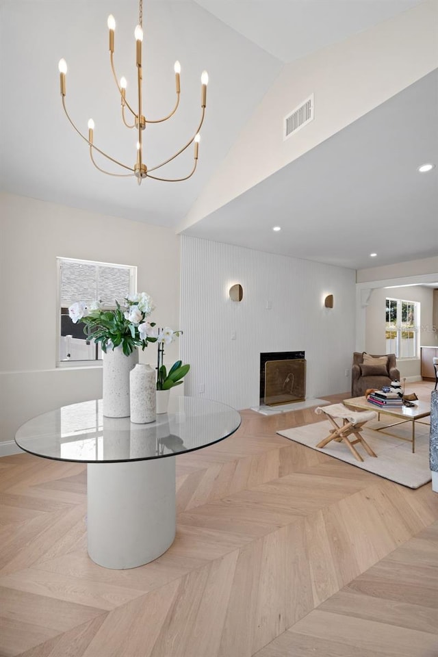 interior space featuring a notable chandelier, visible vents, a fireplace with flush hearth, and high vaulted ceiling