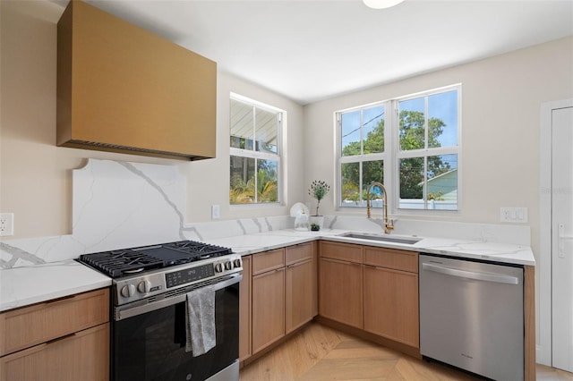 kitchen with wall chimney exhaust hood, a sink, light stone counters, and stainless steel appliances