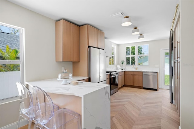 kitchen with light stone countertops, appliances with stainless steel finishes, a sink, visible vents, and a peninsula