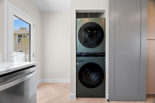 clothes washing area featuring stacked washer and dryer, laundry area, and baseboards