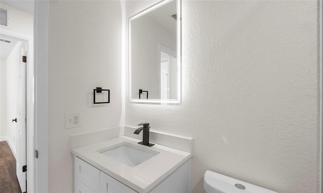half bathroom with toilet, a textured wall, visible vents, and vanity