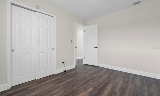 unfurnished bedroom with baseboards, dark wood-style flooring, and visible vents