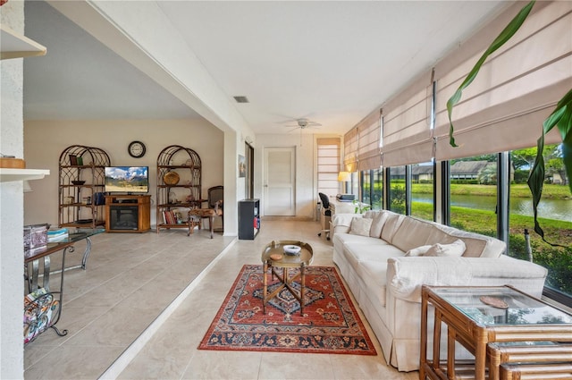 tiled living area with a fireplace, a water view, ceiling fan, and visible vents