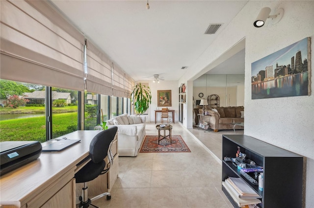 interior space with ceiling fan, visible vents, a water view, and light tile patterned floors