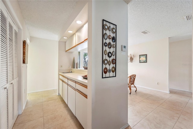 interior space featuring light tile patterned floors, a textured ceiling, visible vents, and a sink