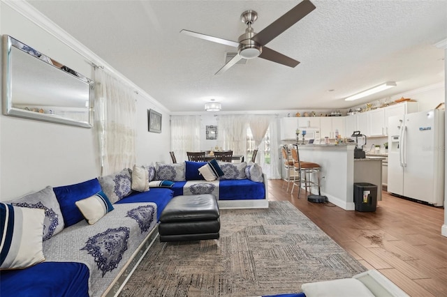 living area with crown molding, a ceiling fan, a textured ceiling, and wood finished floors