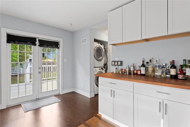 bar featuring dark wood finished floors, stacked washing maching and dryer, baseboards, visible vents, and a bar