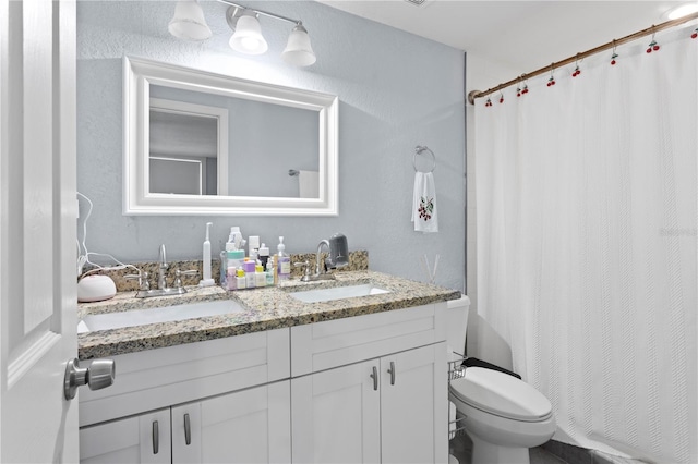 bathroom featuring a textured wall, toilet, double vanity, and a sink
