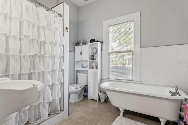 full bathroom featuring tile patterned floors, tile walls, a shower with shower curtain, toilet, and a soaking tub