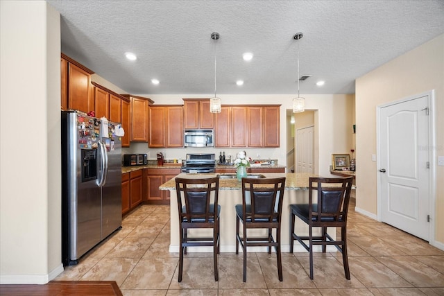 1227 Ballard Green Pl, Brandon, FL 33511 - kitchen with brown cabinets, an island with sink, a breakfast bar area, decorative light fixtures, and appliances with stainless steel finishes