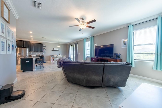 living area with ceiling fan, ornamental molding, light tile patterned flooring, and plenty of natural light