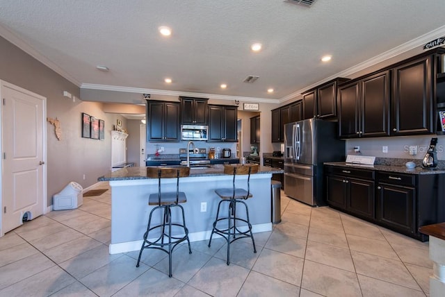 13639 Ashlar Slate Pl, Riverview, FL 33579 - kitchen featuring stainless steel appliances, a breakfast bar area, light tile patterned floors, an island with sink, and ornamental molding