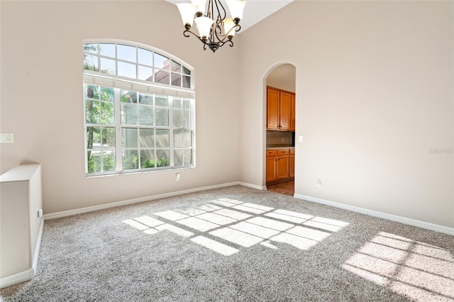 empty room featuring arched walkways, carpet floors, an inviting chandelier, and plenty of natural light