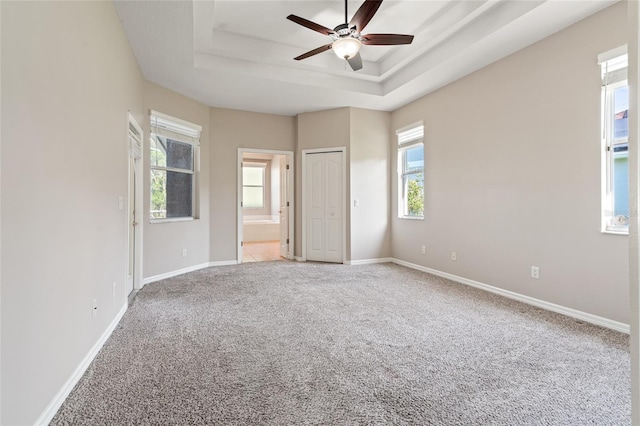 unfurnished bedroom with carpet flooring, a tray ceiling, ensuite bathroom, baseboards, and ceiling fan