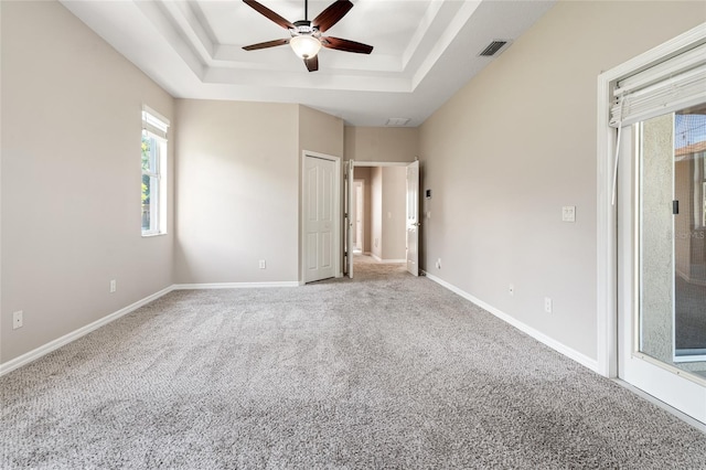 unfurnished bedroom featuring a tray ceiling, visible vents, carpet flooring, and baseboards