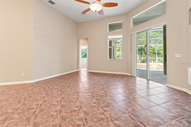 empty room featuring tile patterned floors, visible vents, baseboards, a towering ceiling, and ceiling fan