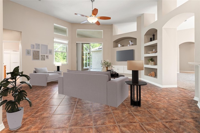 tiled living area featuring baseboards, arched walkways, built in shelves, and ceiling fan