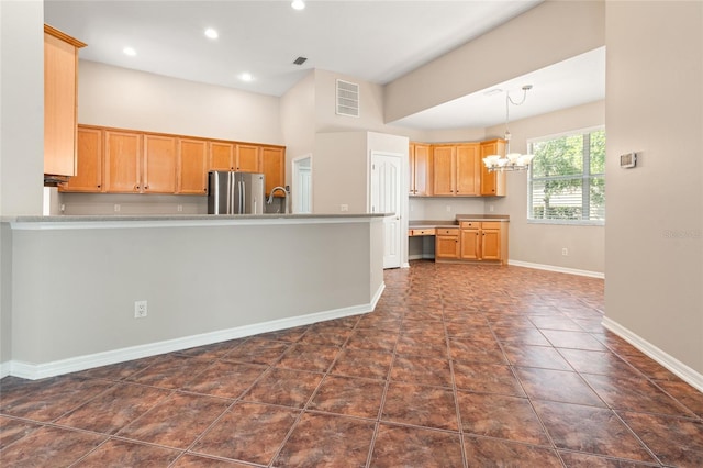 kitchen with a peninsula, visible vents, baseboards, freestanding refrigerator, and a notable chandelier