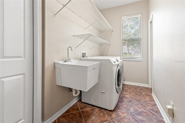 washroom with laundry area, a sink, washing machine and clothes dryer, baseboards, and dark tile patterned flooring