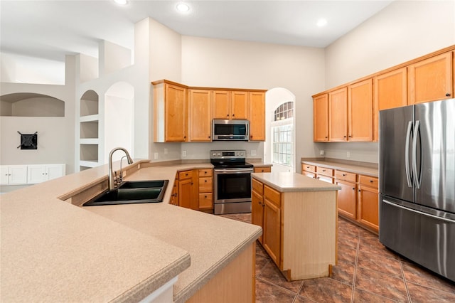 kitchen featuring stainless steel appliances, a peninsula, a sink, a towering ceiling, and light countertops