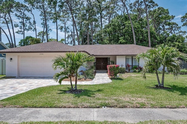 2486 Indian Trl E, Palm Harbor, FL 34683 - ranch-style house featuring a garage, decorative driveway, stucco siding, a front yard, and roof with shingles