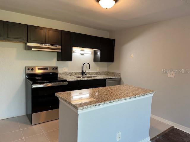kitchen featuring stainless steel appliances, a sink, light stone counters, under cabinet range hood, and a kitchen island