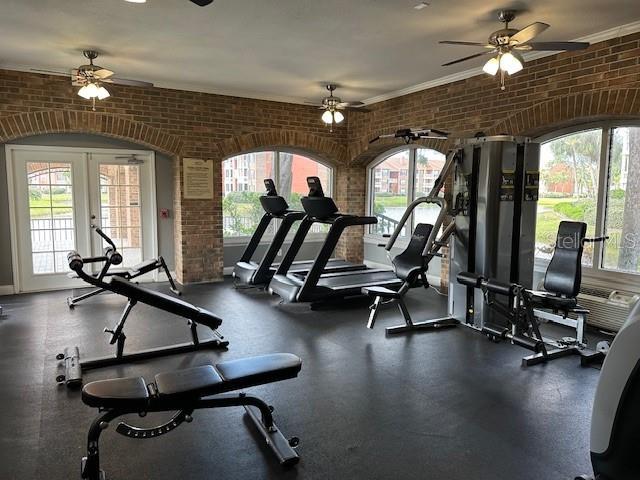 workout area featuring ceiling fan, crown molding, brick wall, and french doors