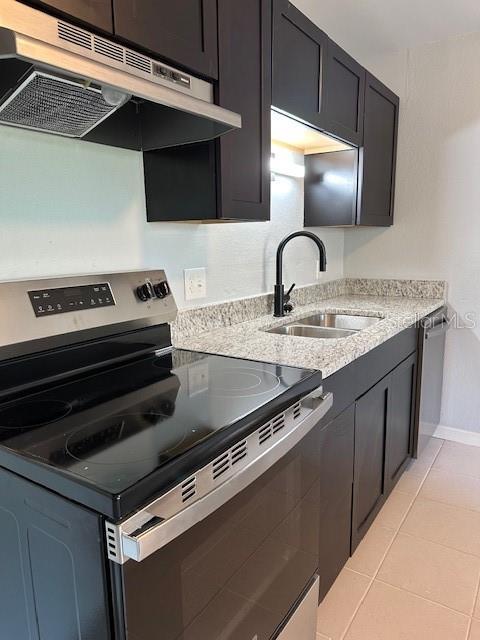 kitchen with a sink, light tile patterned floors, appliances with stainless steel finishes, baseboards, and under cabinet range hood