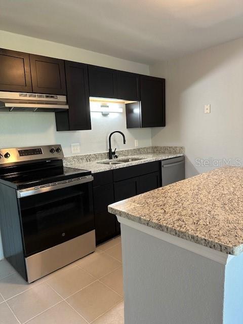 kitchen featuring a sink, light tile patterned flooring, appliances with stainless steel finishes, under cabinet range hood, and light stone countertops