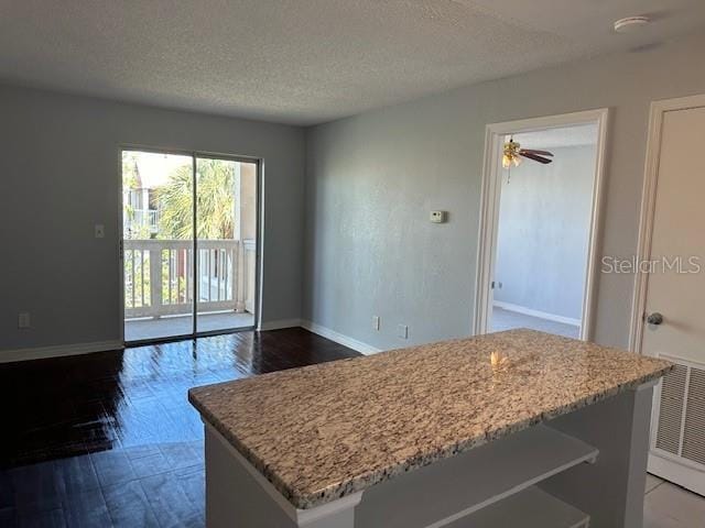 interior space with a textured ceiling, a kitchen island, light stone countertops, and baseboards