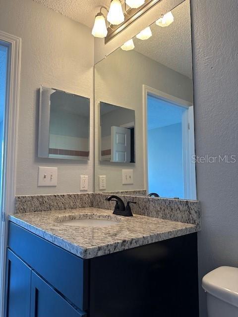 bathroom with a textured wall, vanity, a textured ceiling, and toilet