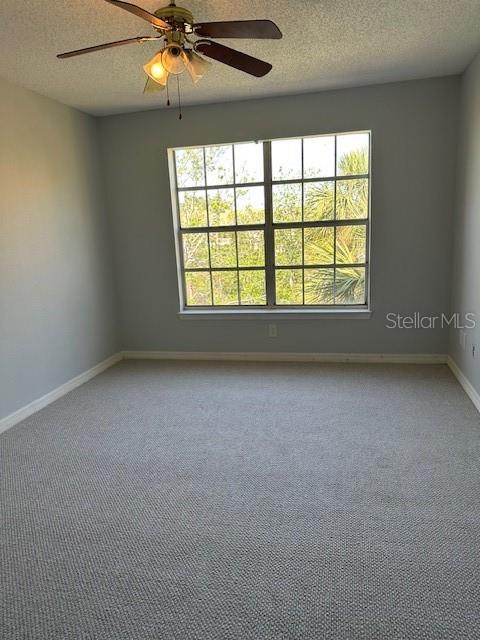 empty room featuring light carpet, a ceiling fan, baseboards, and a textured ceiling
