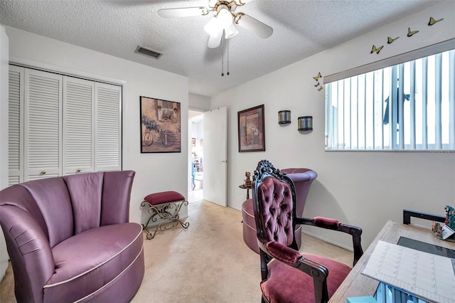 carpeted home office with a textured ceiling, a ceiling fan, and visible vents