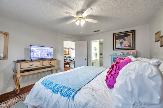 bedroom with a textured ceiling, ensuite bath, a ceiling fan, visible vents, and wood finished floors
