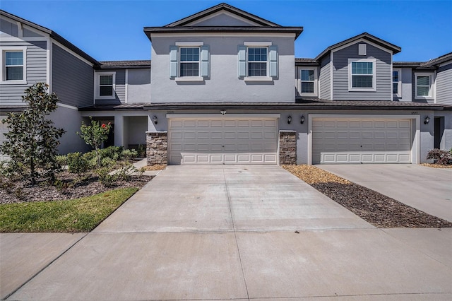view of property featuring an attached garage, driveway, stone siding, and stucco siding